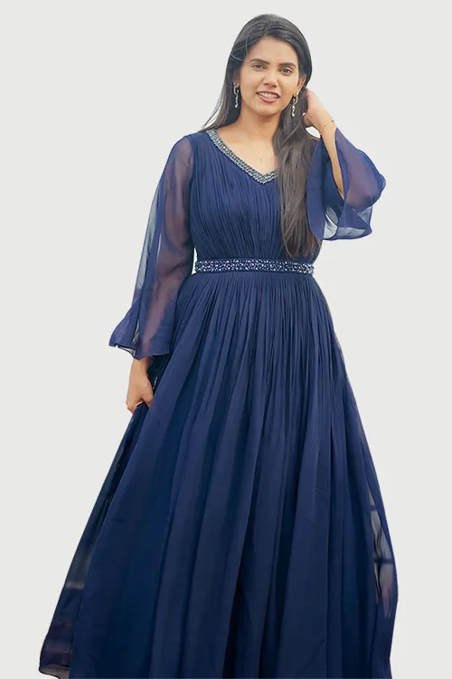 The navy Pleated Gown at full length, the pleating running from the shoulder to the floor, with sheer flared sleeves and a beaded belt