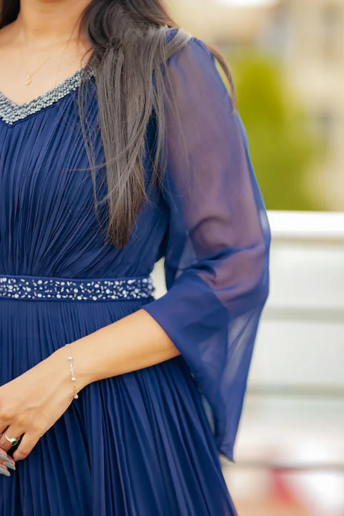 A close view of the Pleated Gown's sheer navy bell sleeve and the beaded belt sitting on the pleats at the waist
