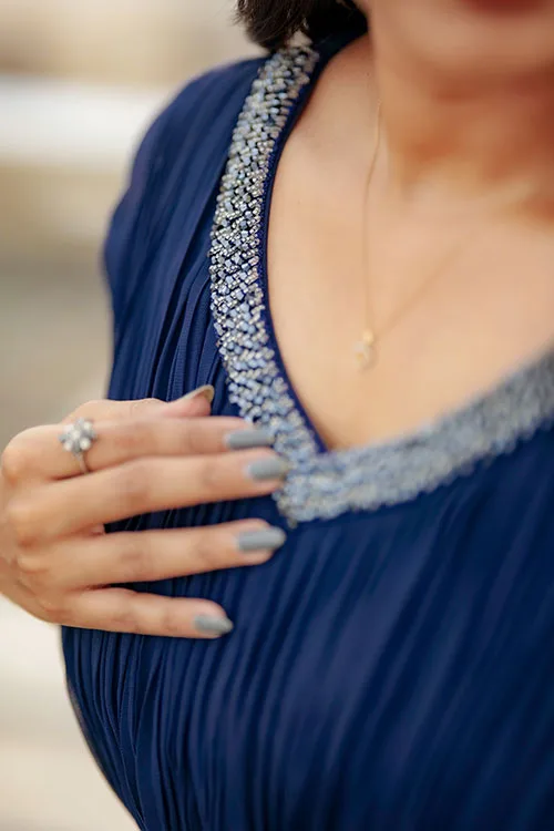 A close view of the Pleated Gown's neckline, a band of silver beadwork following the V against the navy pleats